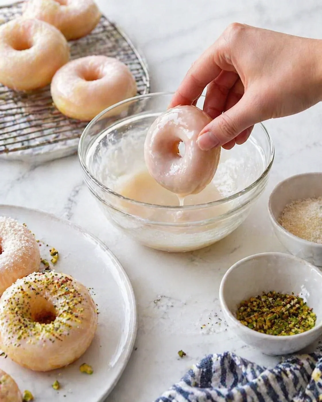 Cooled mochi donut being dipped into glossy glaze, then sprinkled with colorful toppings.
