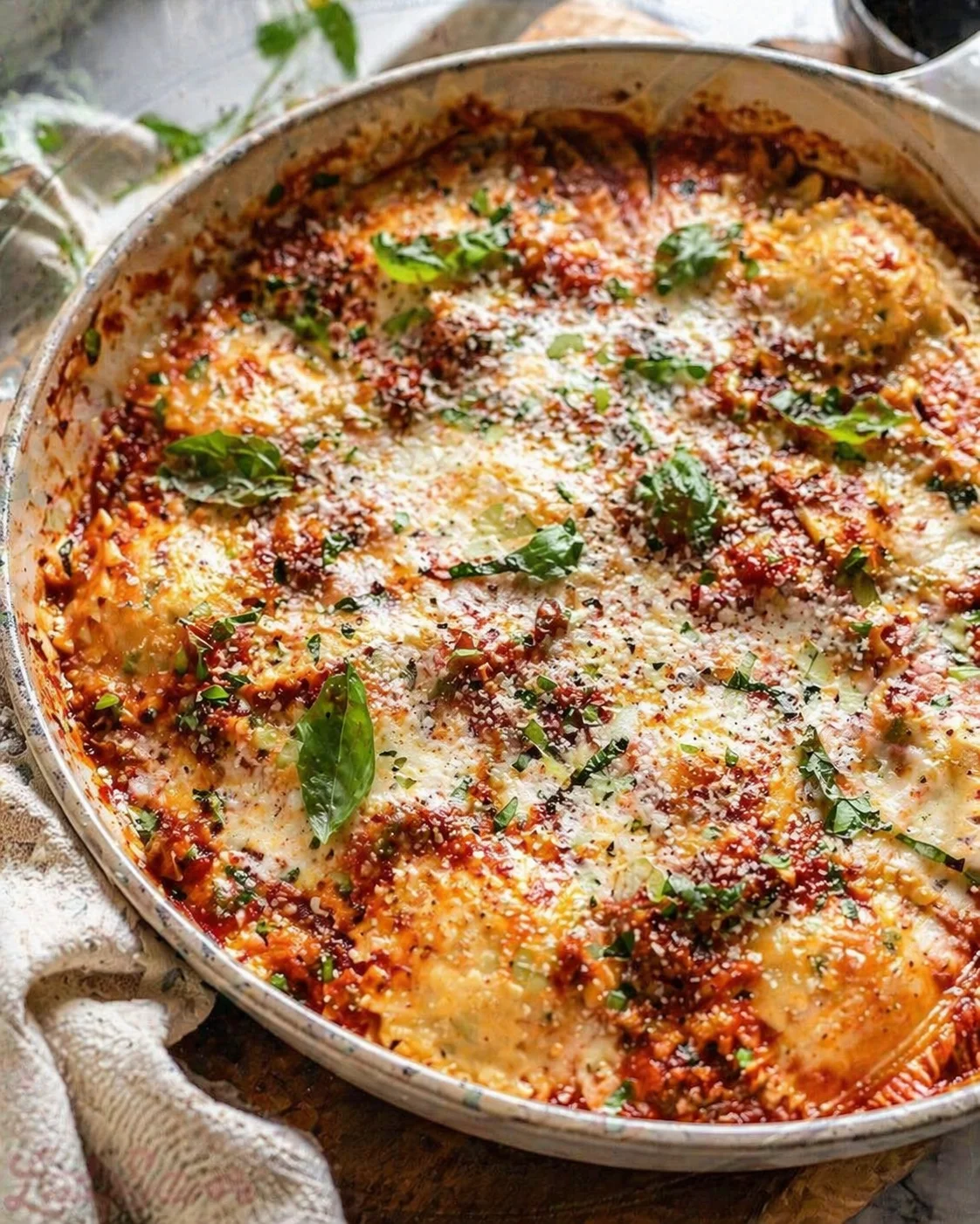 round pan of bubbling cheesy tomato bake topped with fresh basil leaves