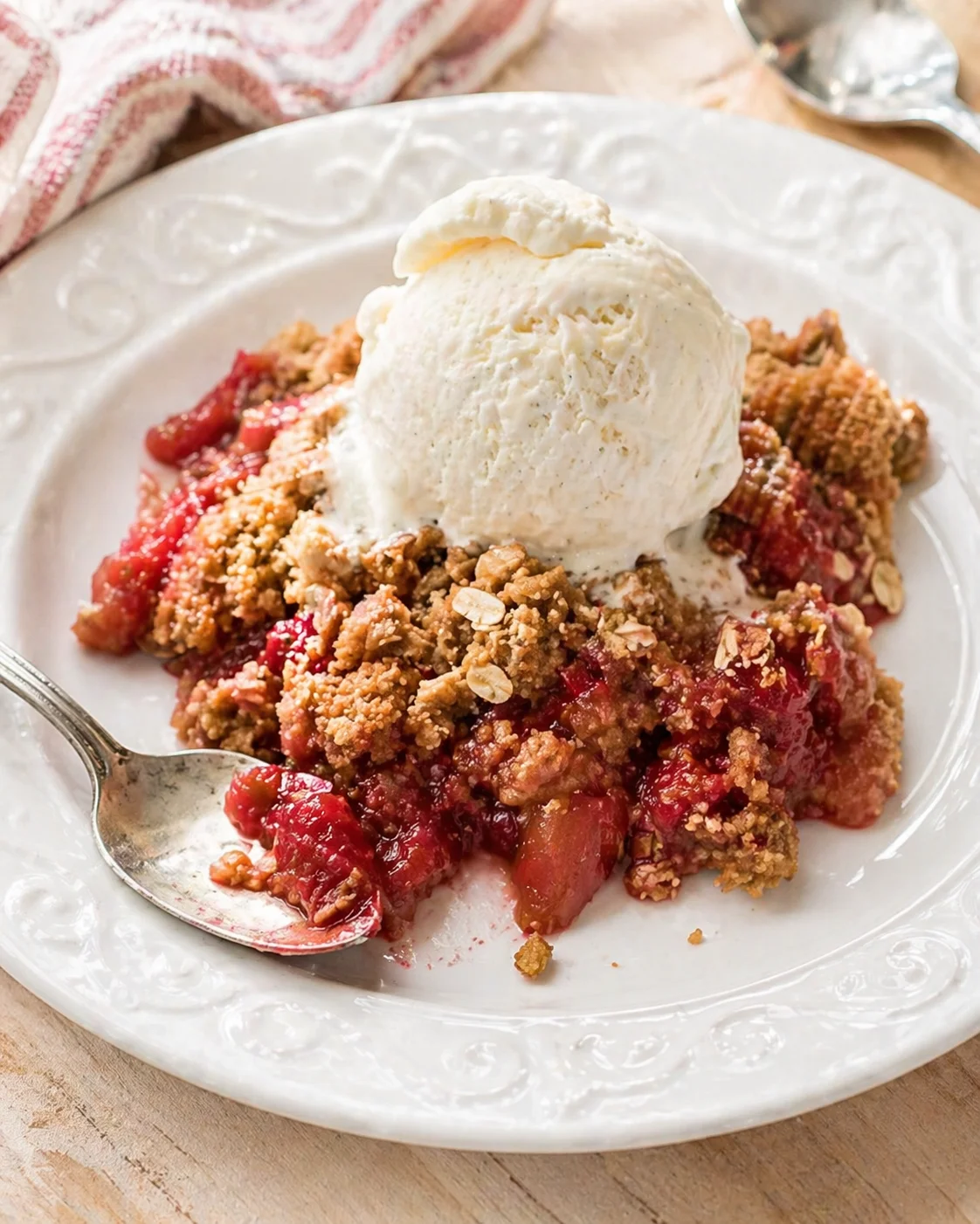 Decorated white plate with warm berry crumble and a scoop of vanilla ice cream