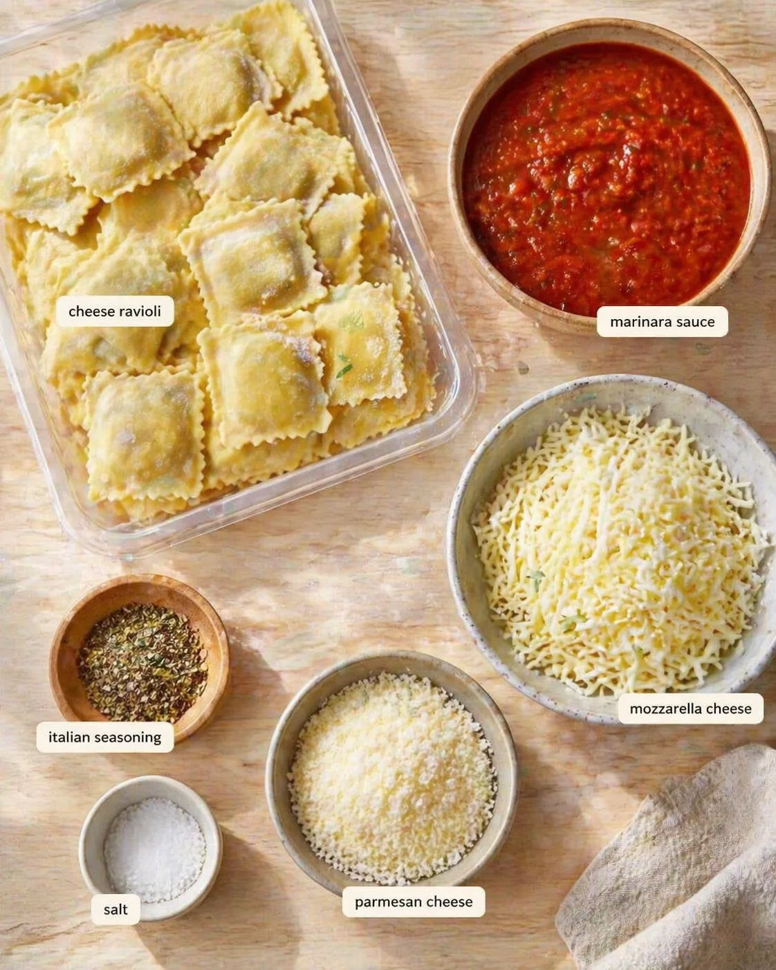 Top-down view of cheese ravioli, marinara sauce, and cheeses on a wooden table.