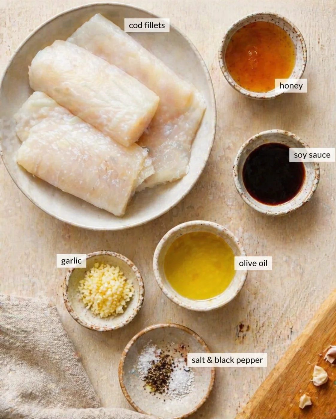 Top-down view of cod fillets with labeled bowls of honey, soy sauce, garlic, olive oil, salt, and pepper.