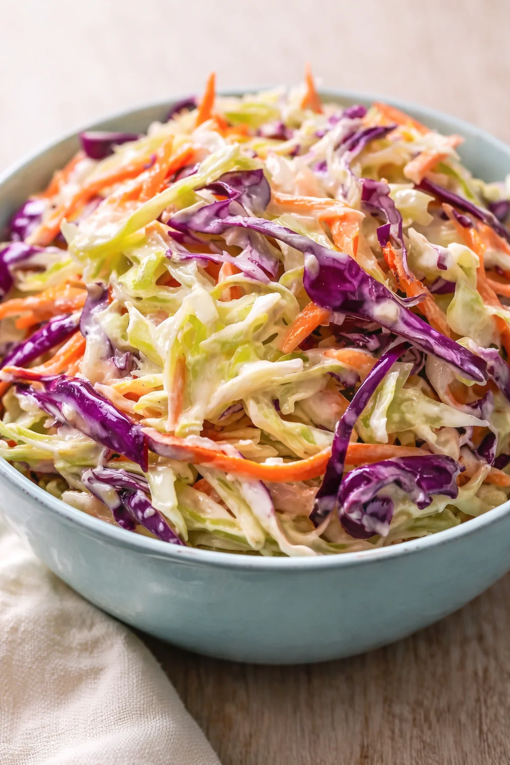 bowl of colorful shredded cabbage and carrot coleslaw in a light blue bowl on a wooden table
