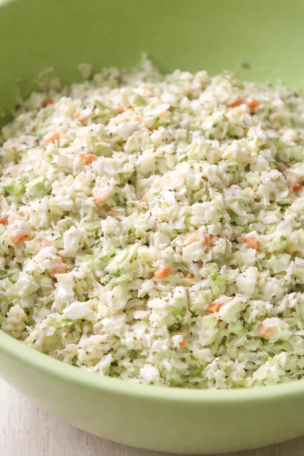 close-up of a light-green bowl filled with finely chopped creamy coleslaw (cabbage, carrot, celery)