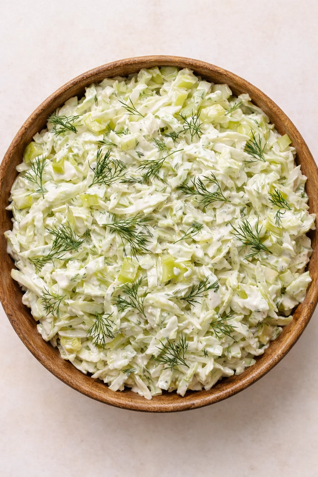 Top-down view of creamy celery salad in a wooden bowl on a light surface