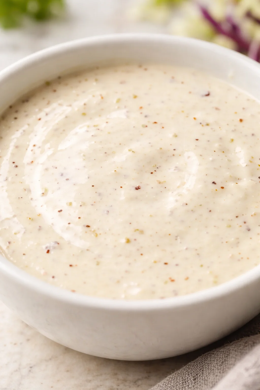 White bowl of creamy sauce with pepper flecks on a marble surface