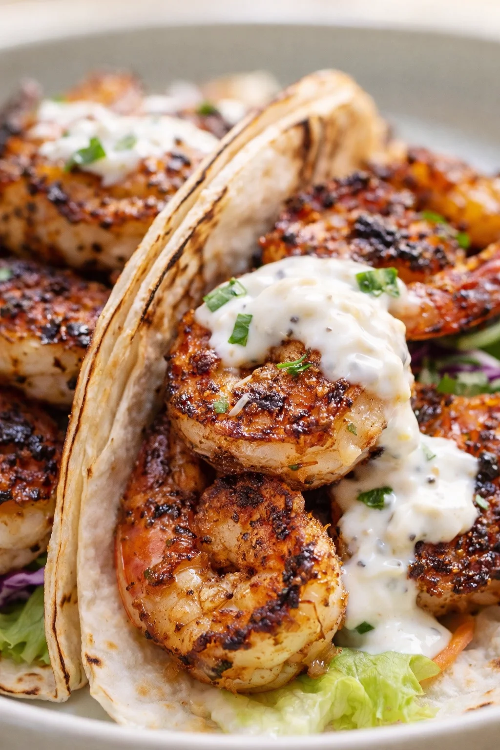 close-up of grilled shrimp tacos topped with creamy herb sauce and tortilla wedges.