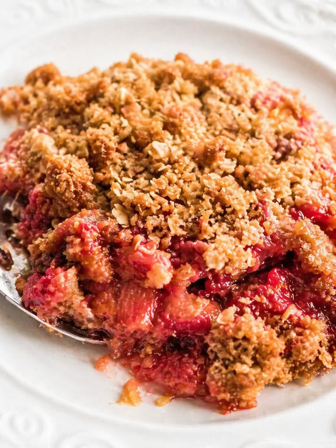Close-up of a warm fruit crumble with golden crumb topping on a white plate.