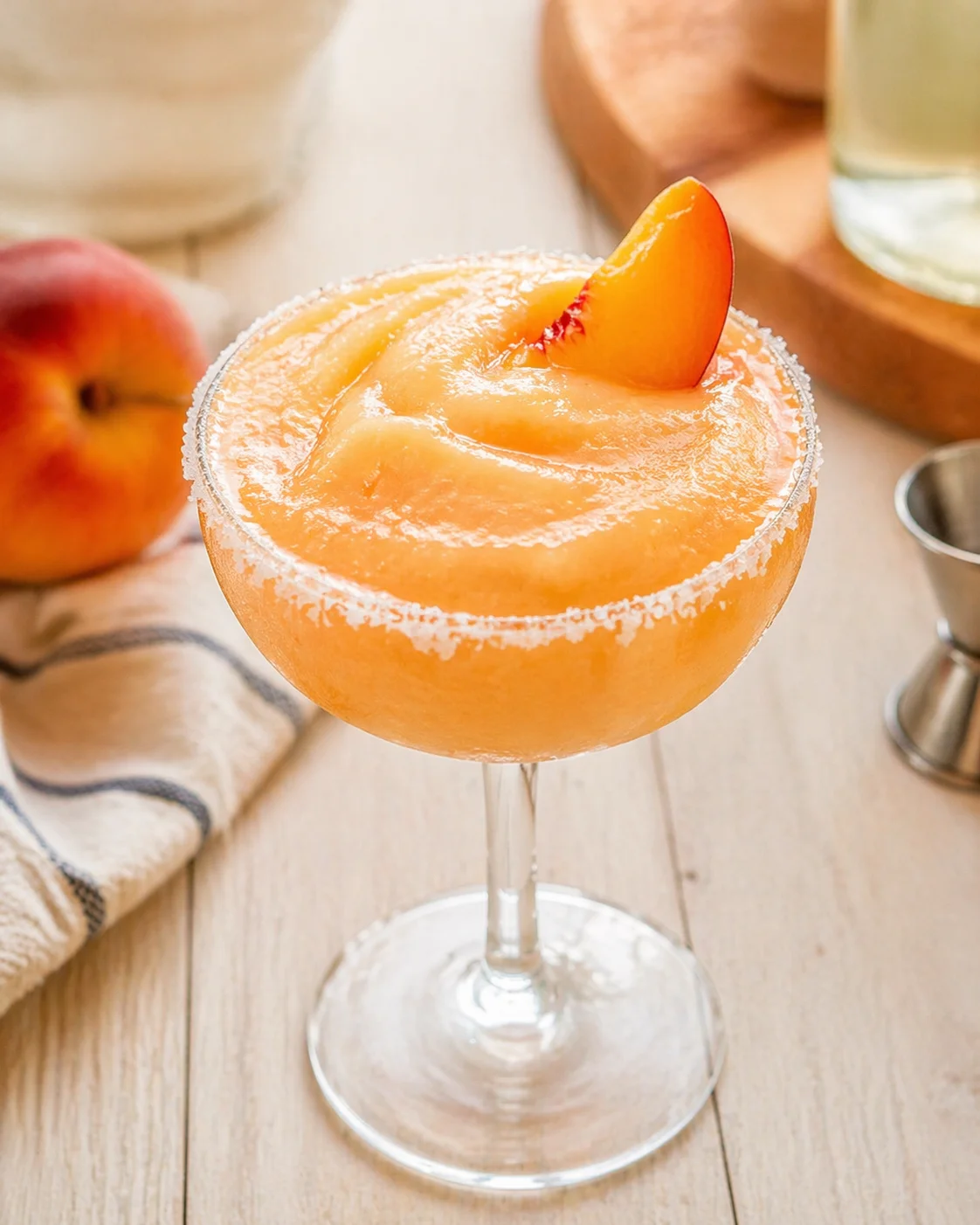 peach-colored cocktail in a salted-rim coupe with peach slice garnish.