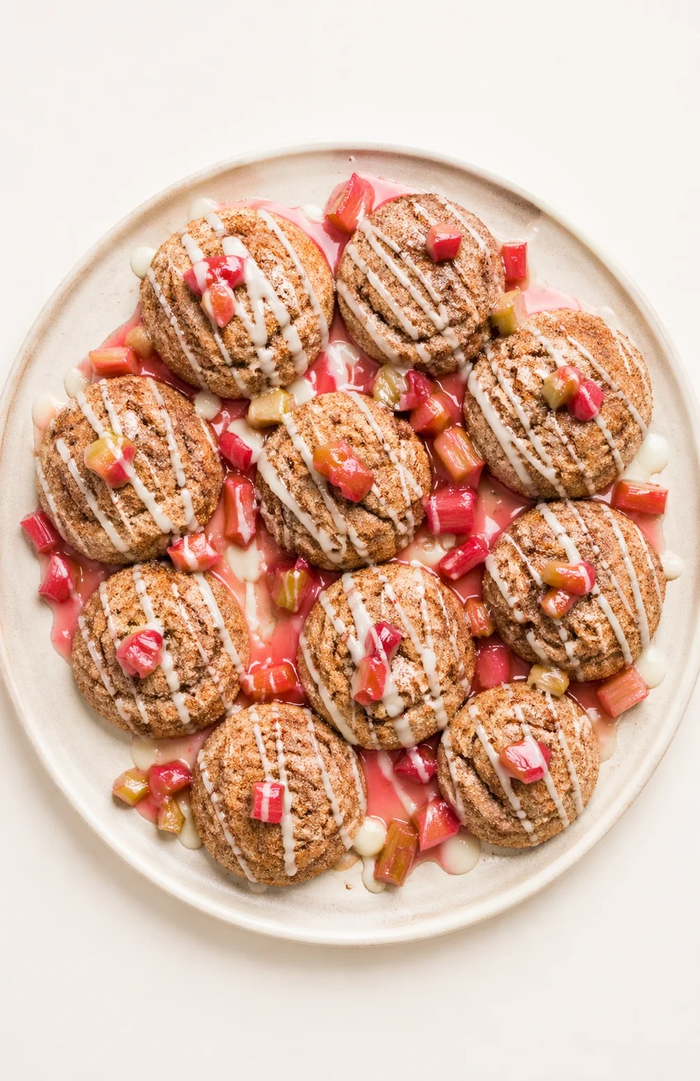 oval beige plate with round, glaze-drizzled cookies surrounded by pink sauce and rhubarb chunks
