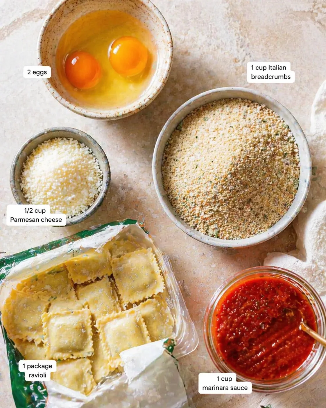 Top-down view of ravioli ingredients on a counter: eggs, parmesan, breadcrumbs, marinara, and packaged ravioli