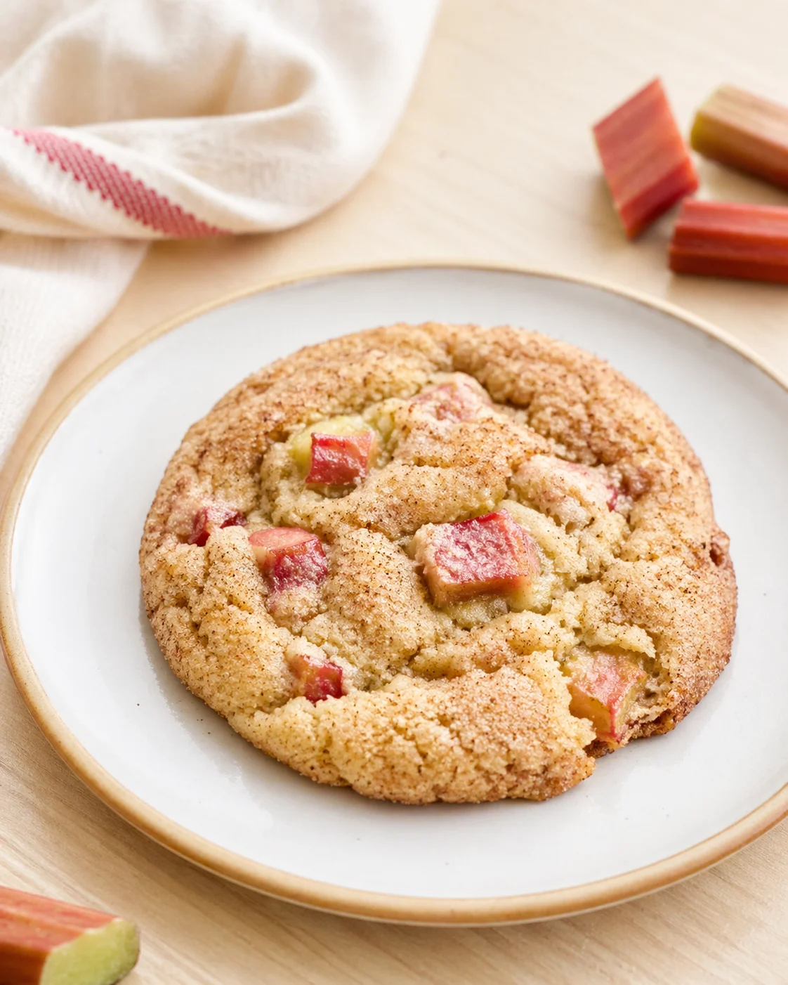 round golden rhubarb cookie on a white plate with rhubarb chunks nearby
