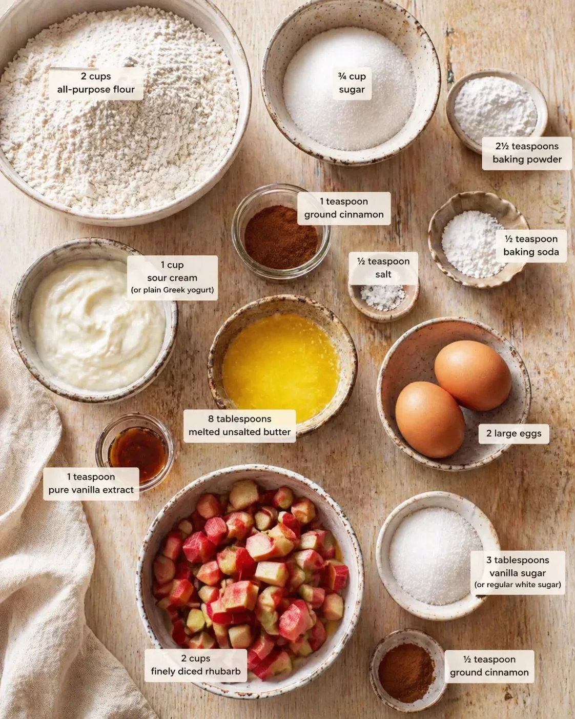 top-down view of labeled baking ingredients arranged on a wooden table with rhubarb, flour, eggs, butter, and sugar