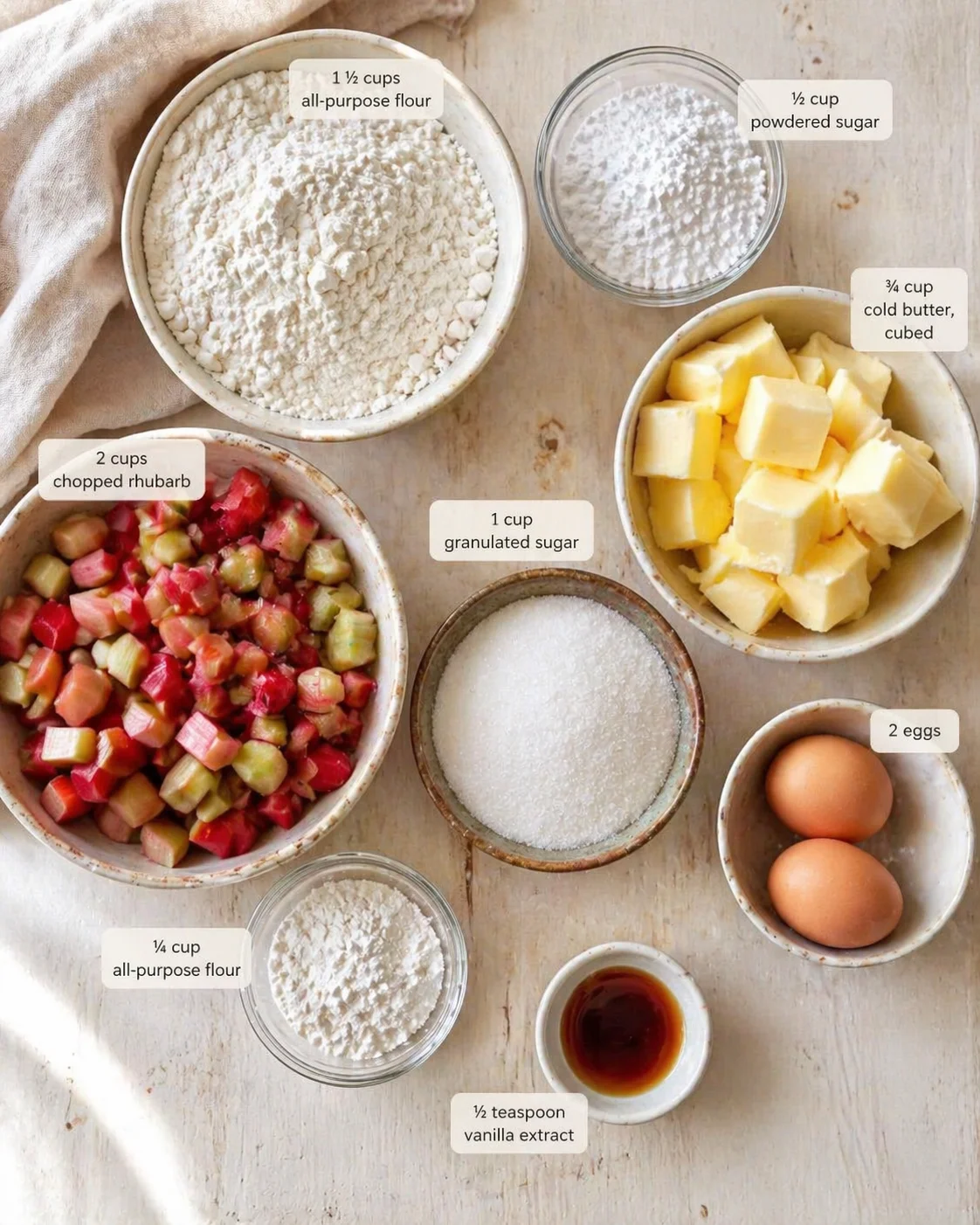 Overhead view of rhubarb, flour, sugar, butter, eggs, and vanilla extract with labeled measurements.