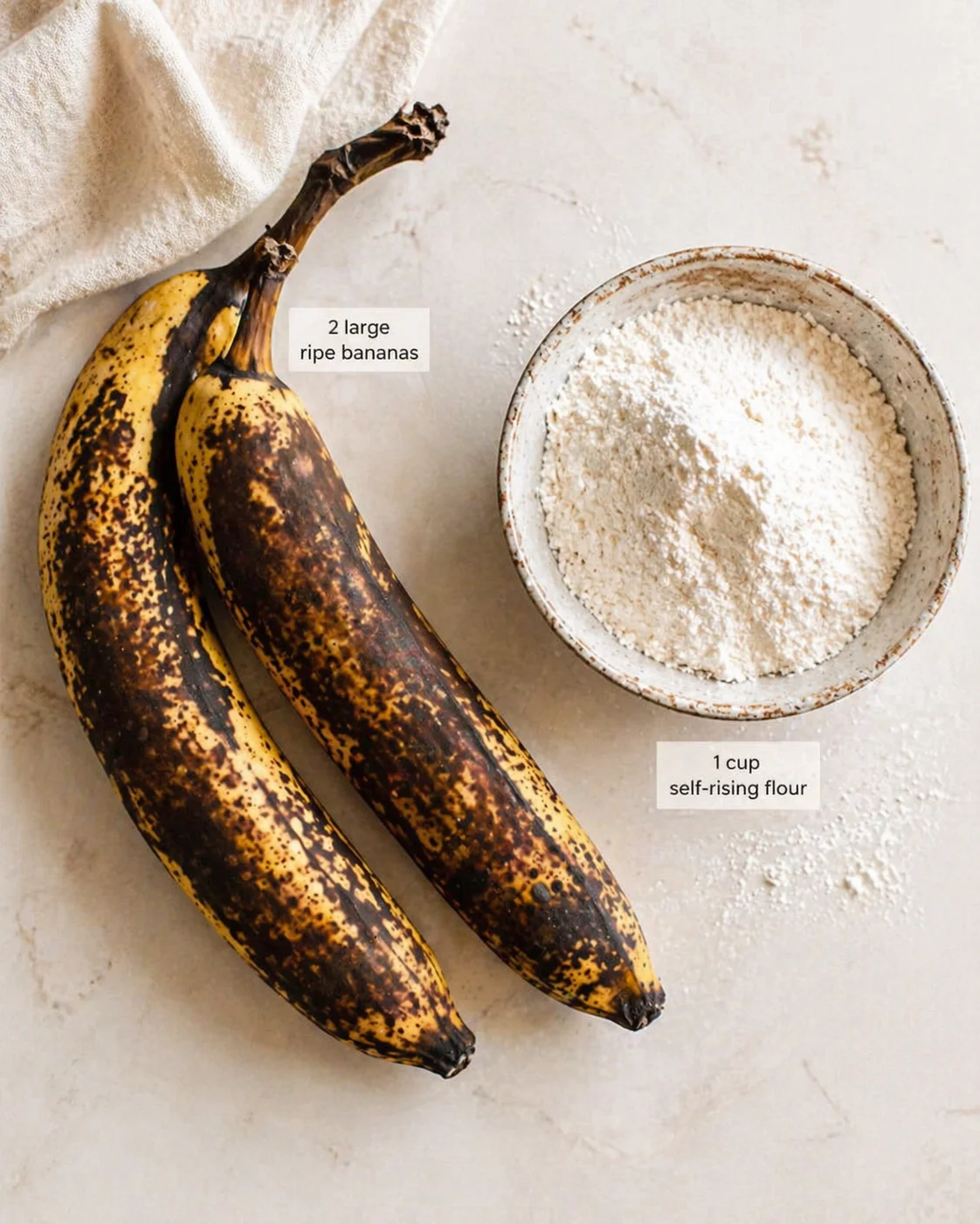 Two speckled ripe bananas beside a bowl of self-rising flour on a light countertop.