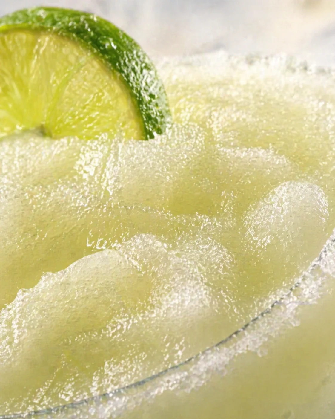 Close-up of a sugar-rimmed glass with a lime wedge, ice, and pale-green cocktail