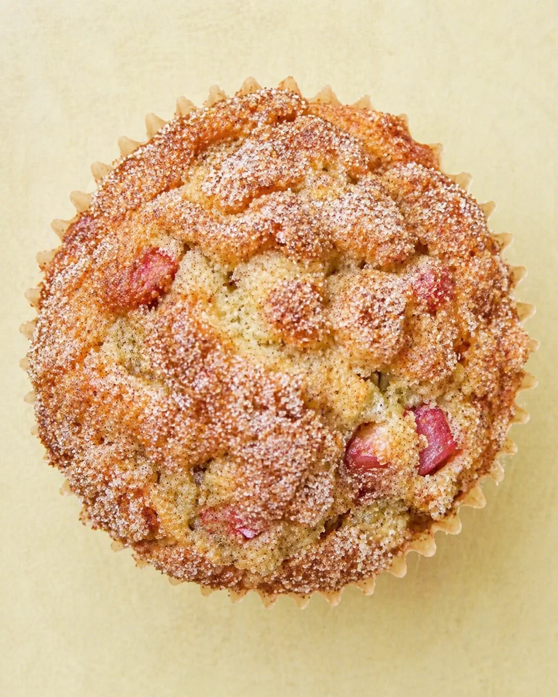 top-down view of a golden-brown streusel muffin with pink berries on a pale-yellow background