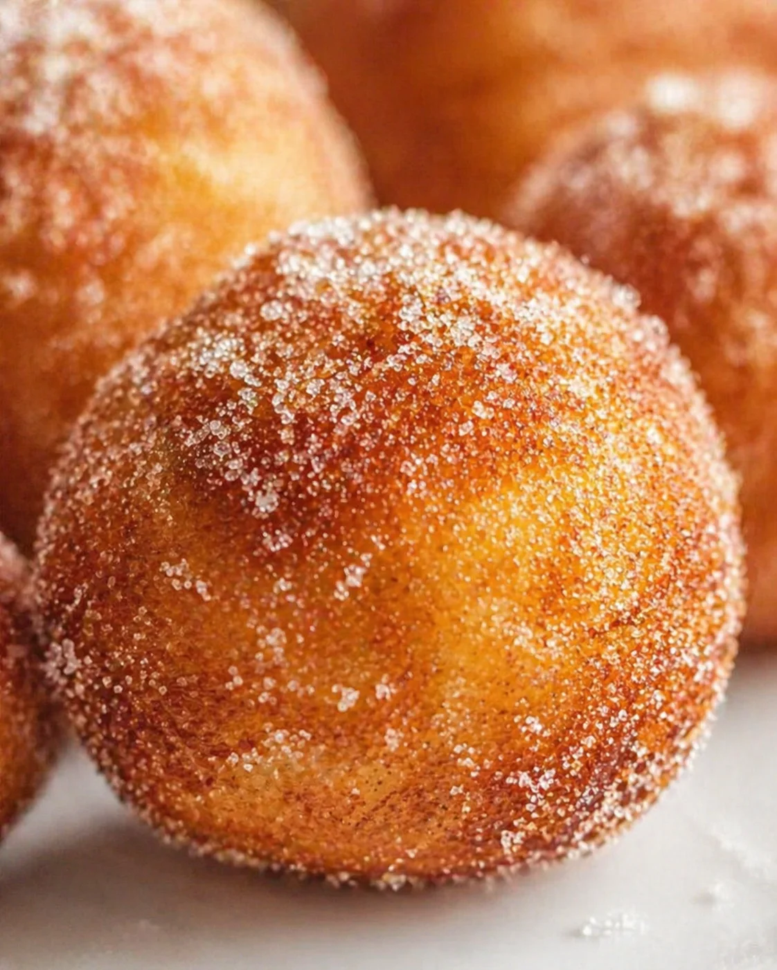 Close-up of golden brown sugar-dusted doughnut holes piled on a white surface.