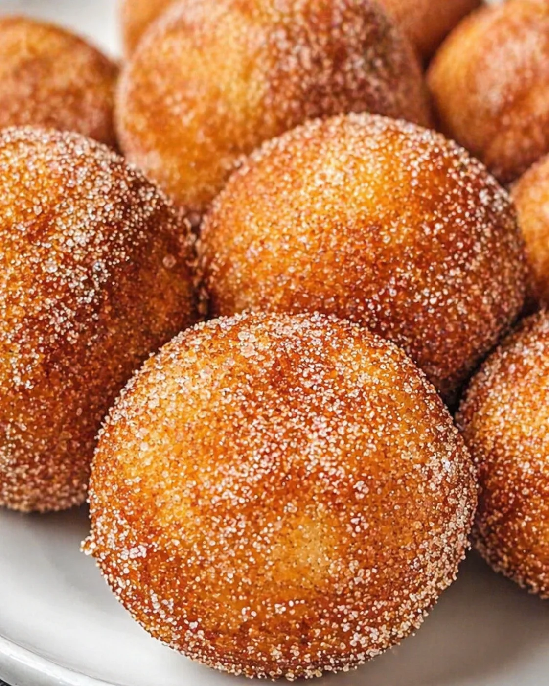 Close-up of golden brown sugar-dusted fried dough balls piled on a white plate.