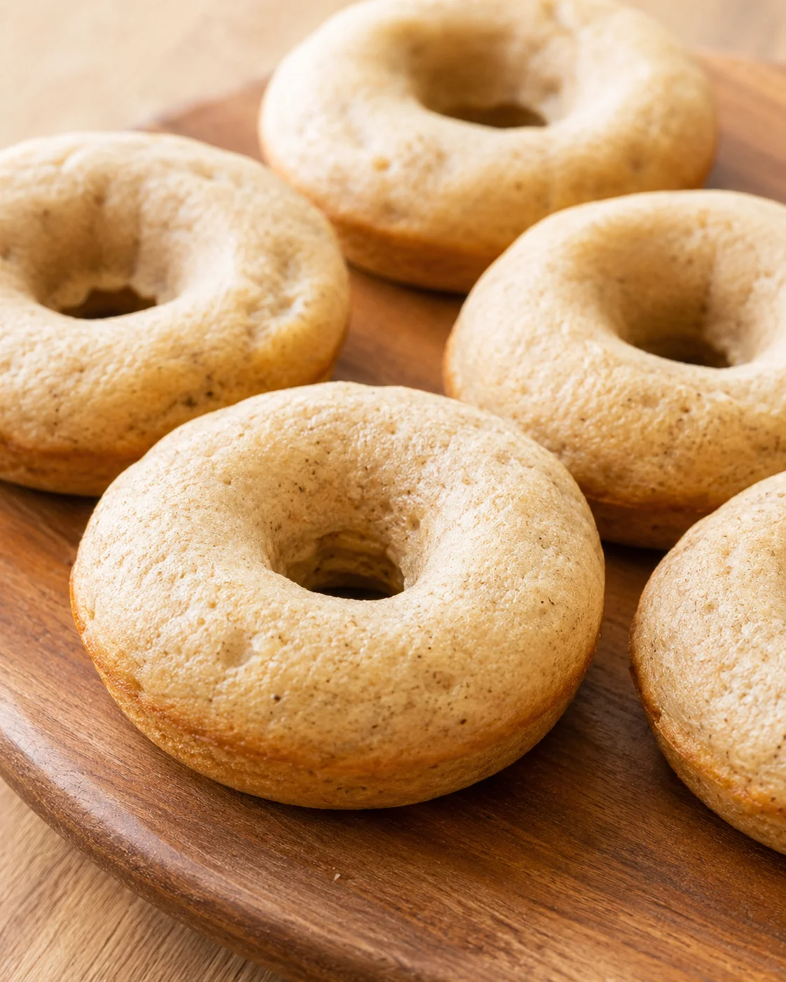 Several light-brown bagels with a shiny crust arranged on a round wooden board.