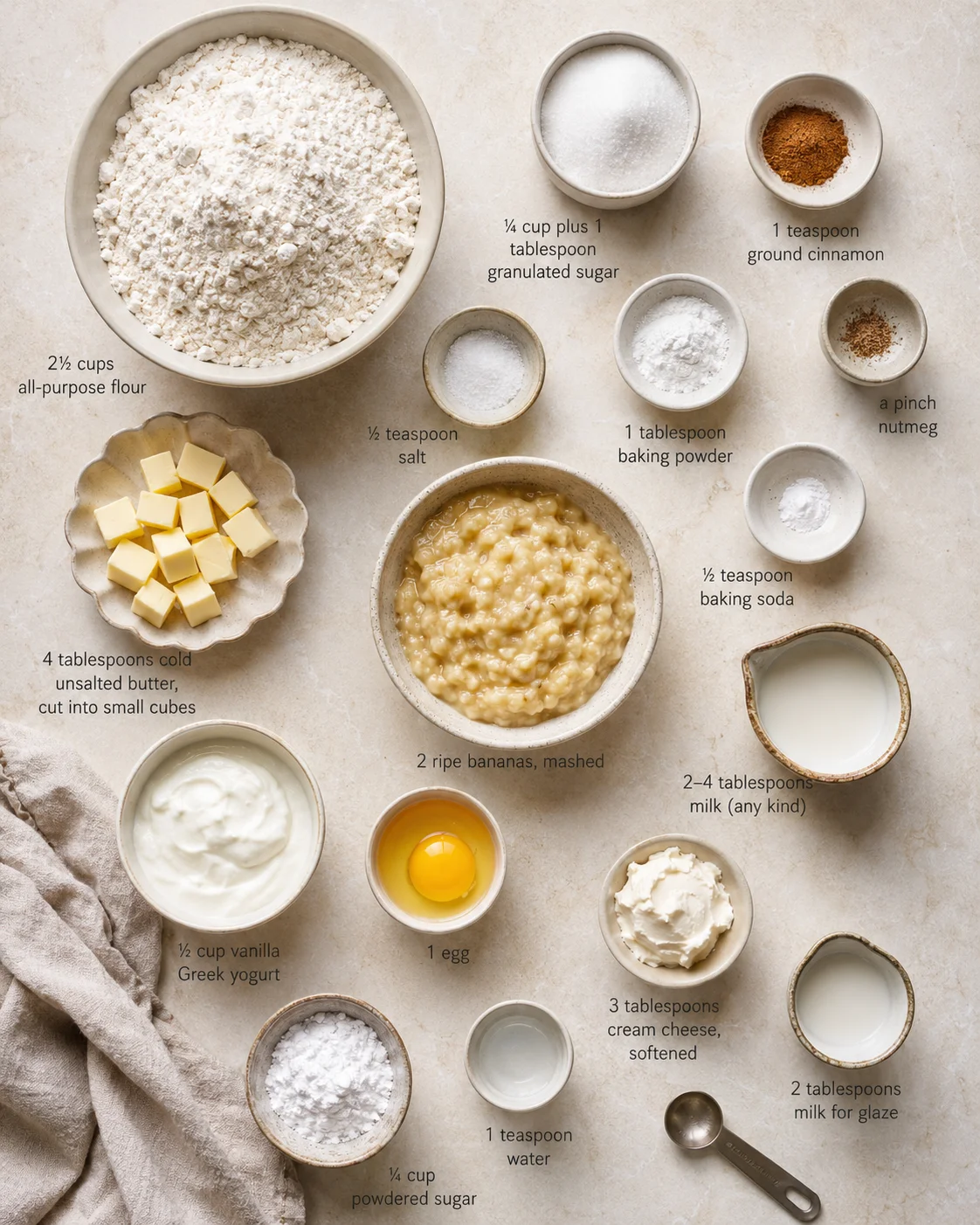 Overhead shot of baking ingredients arranged with labeled measurements: flour, butter, sugar, spices, eggs, bananas, milk and yogurt.
