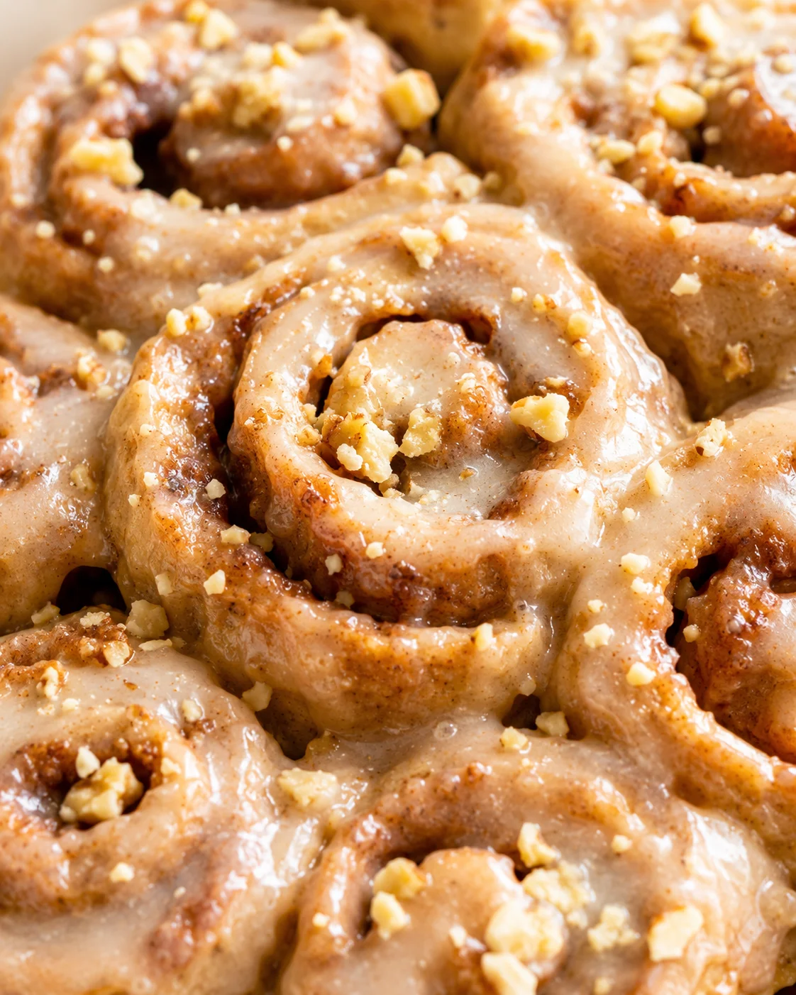 close-up of glazed cinnamon rolls topped with crushed nuts and a glossy syrup