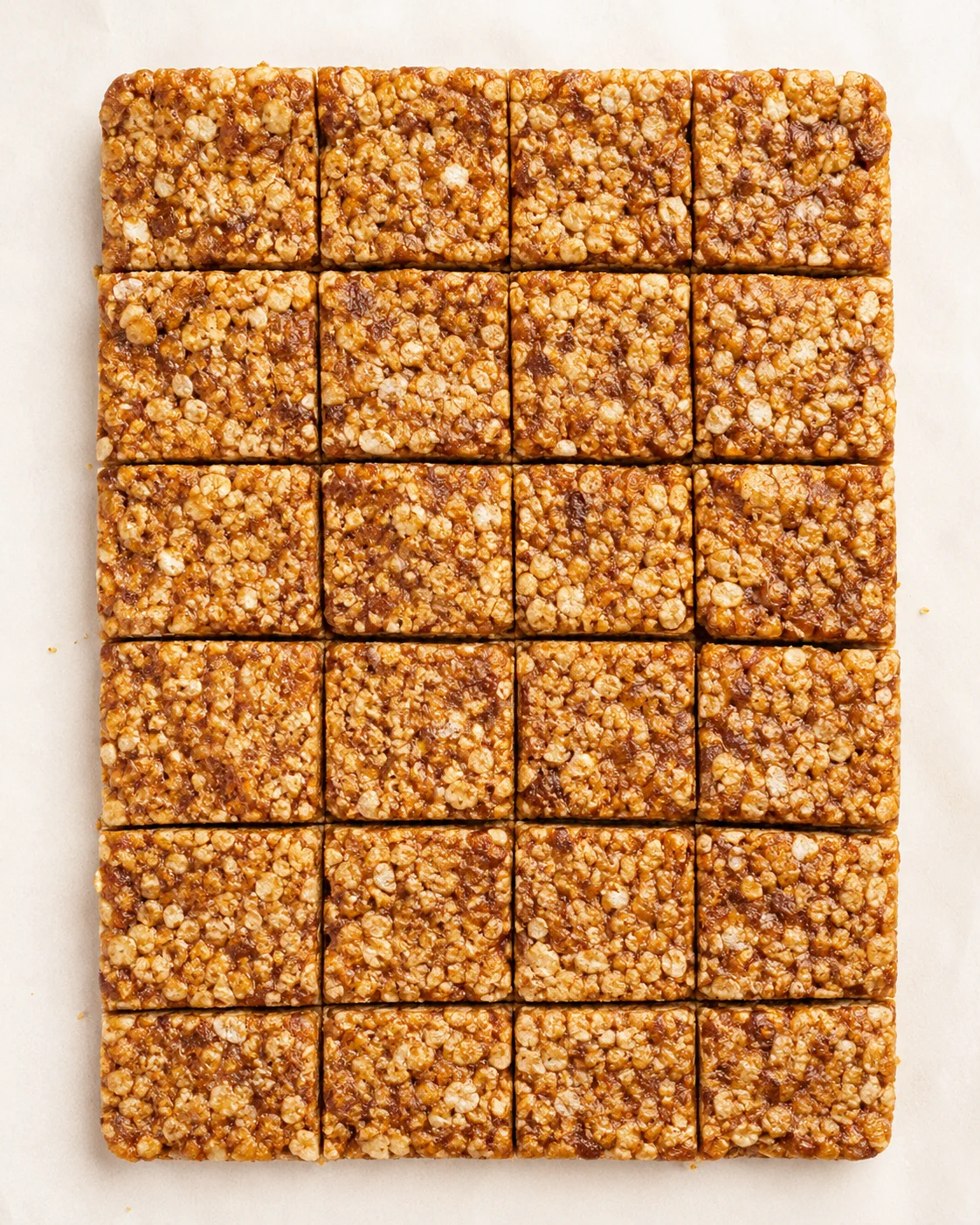 Top-down view of a parchment-lined sheet with uniform granola bars, nuts and oats visible