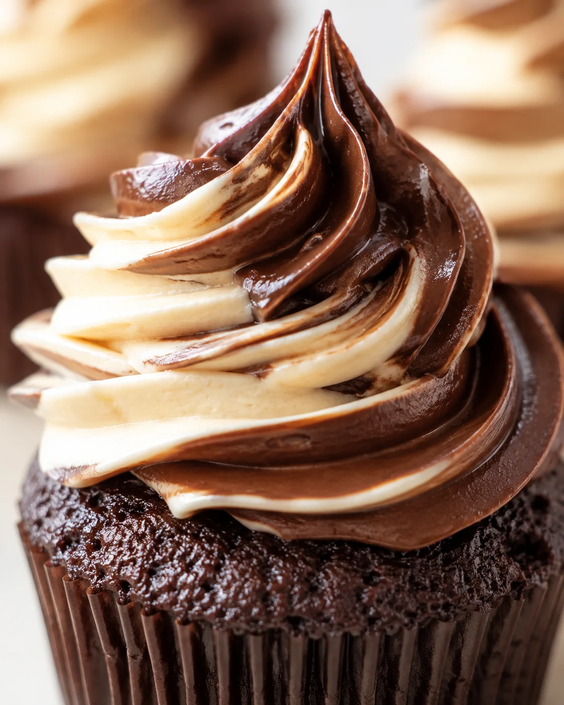 Close-up of a chocolate cupcake topped with a glossy chocolate-vanilla swirl frosting.