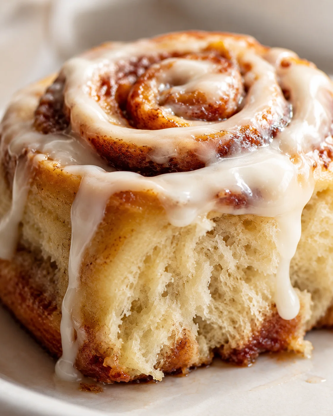 Close-up of a cinnamon roll with glossy white icing dripping down sides.