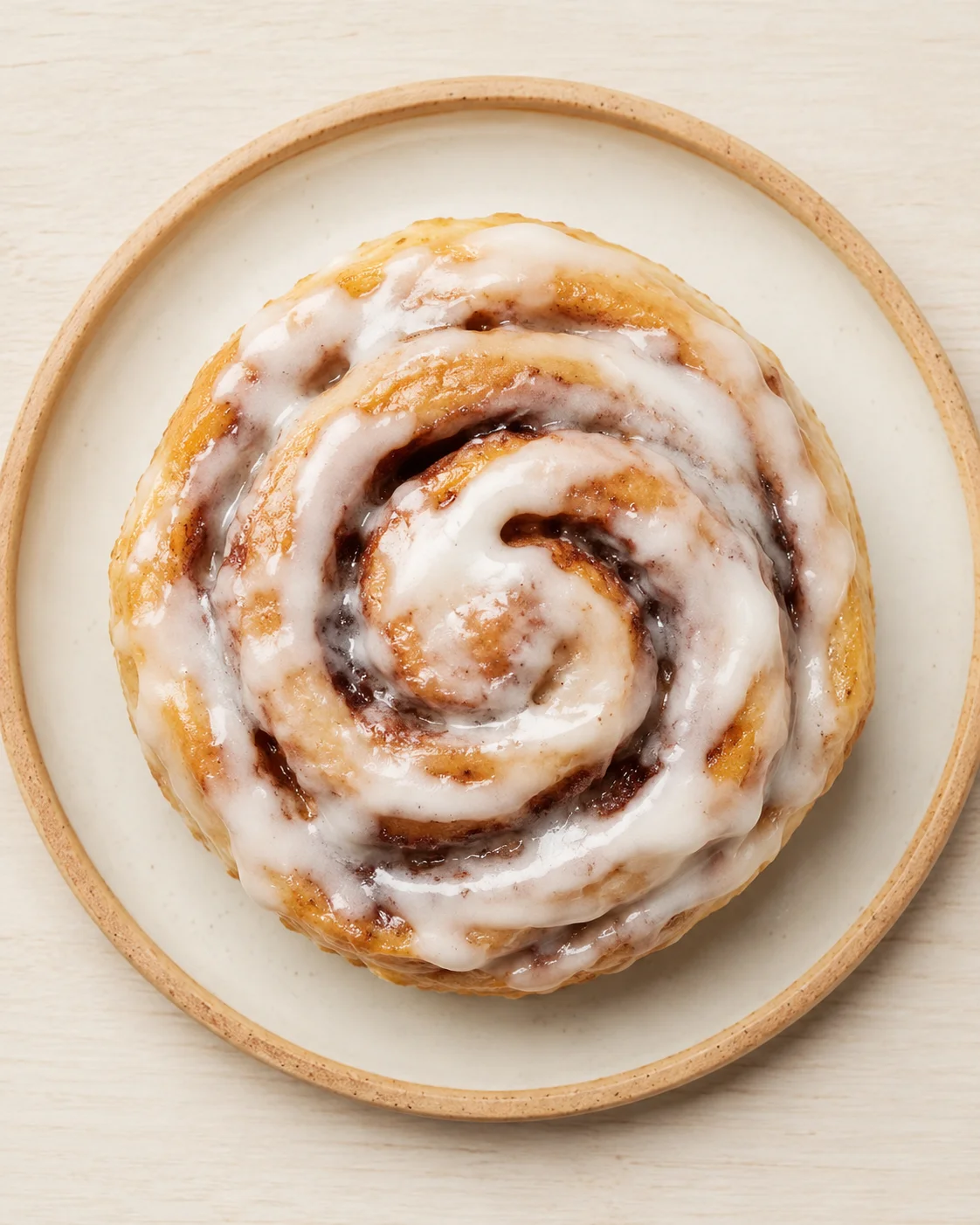 top-down view of a glazed cinnamon roll on a beige plate, warm wooden surface