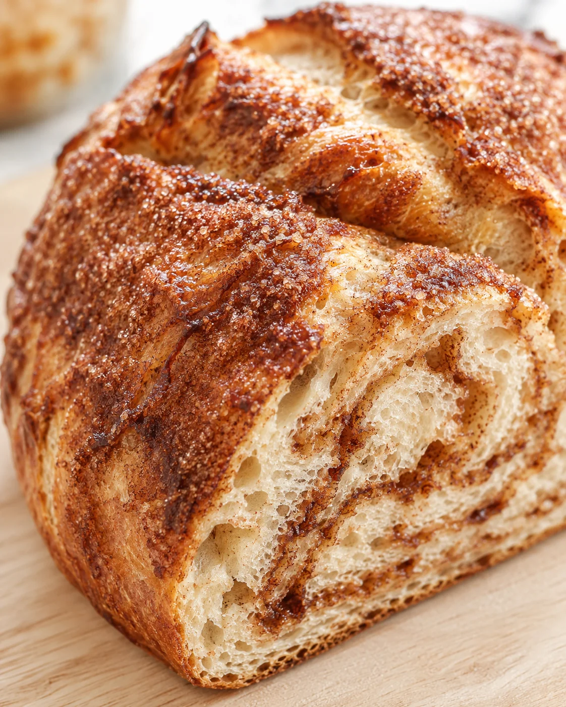 Close-up of a golden-brown cinnamon-swirled bread loaf on a wooden board.