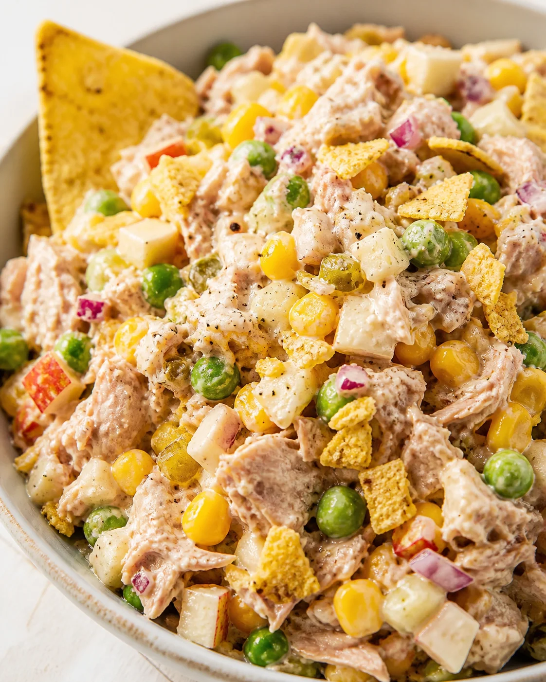 bowl of creamy chicken salad with corn, peas, red onion, diced white cubes, and tortilla chips