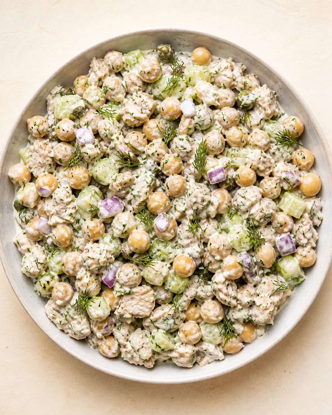 top-down view of a large bowl of creamy chickpea salad with cucumbers, red onions, and dill