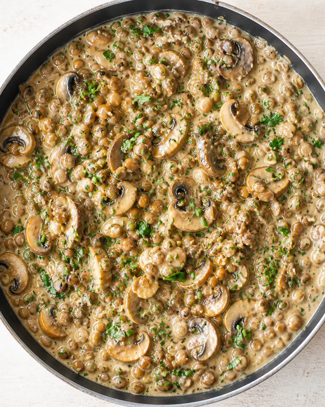 Creamy mushroom and lentil dish in a skillet, garnished with parsley.