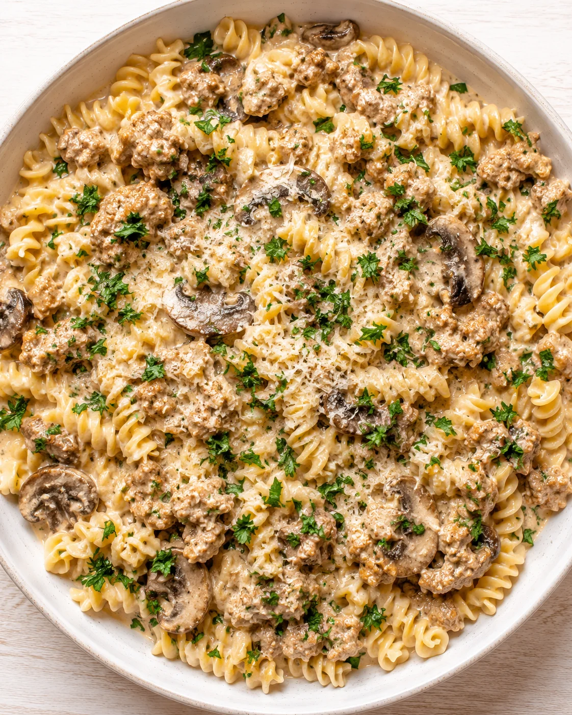 Creamy mushroom pasta with ground meat, parsley garnish, in a round white bowl.