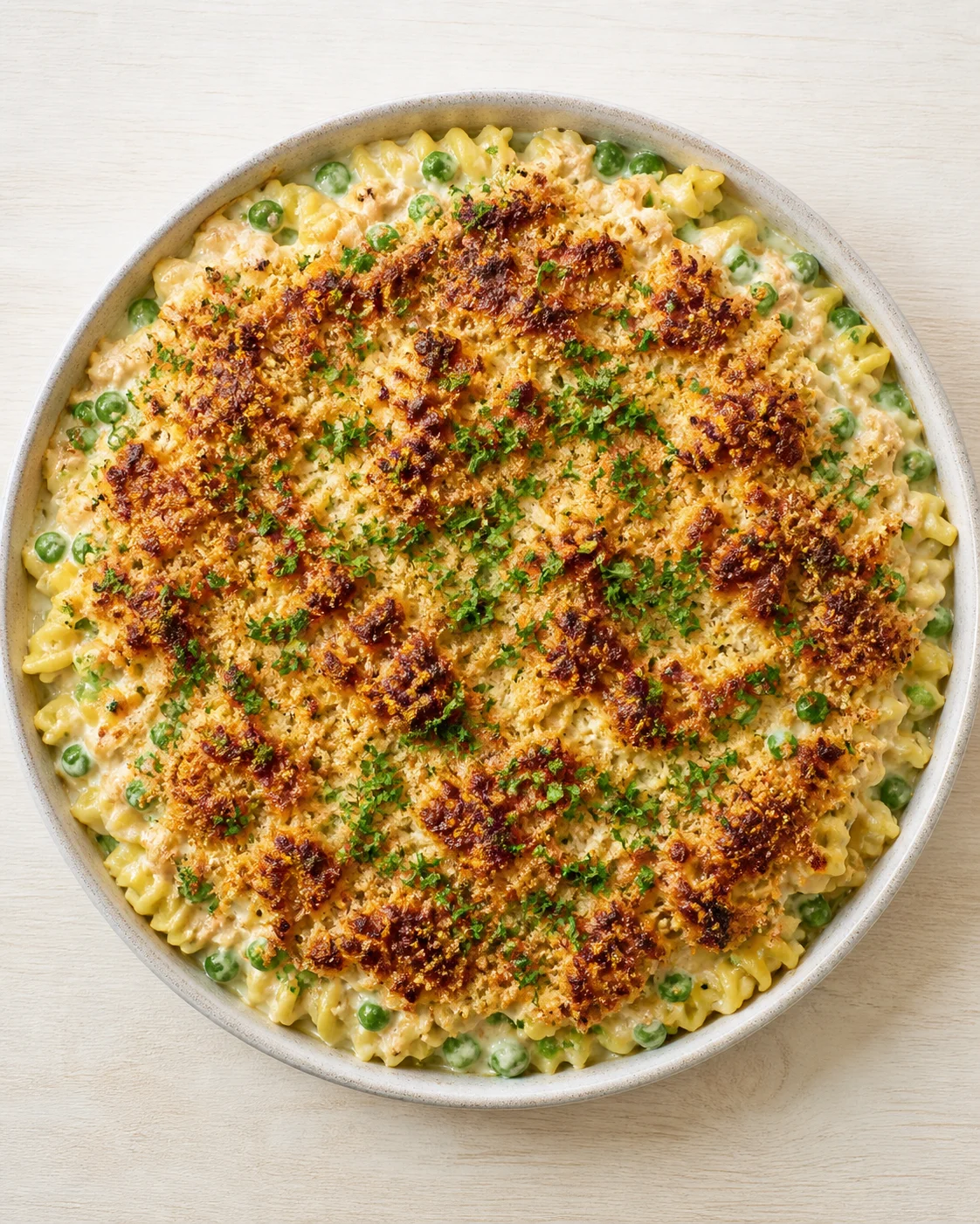 round baking dish of creamy macaroni and cheese with peas, topped with golden breadcrumbs