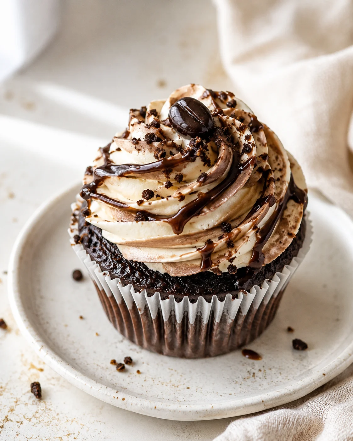 Chocolate cupcake with a tall vanilla buttercream frosting swirl, chocolate drizzle, and cookie crumb topping on a white plate.