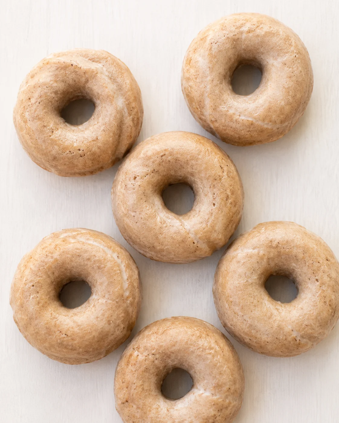 Seven plain ring donuts arranged in a cluster on a light wooden surface