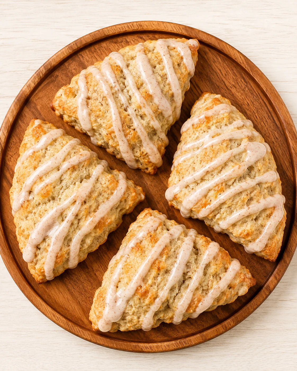 top-down view of four triangular scones on a round wooden board, with white glaze drizzle.