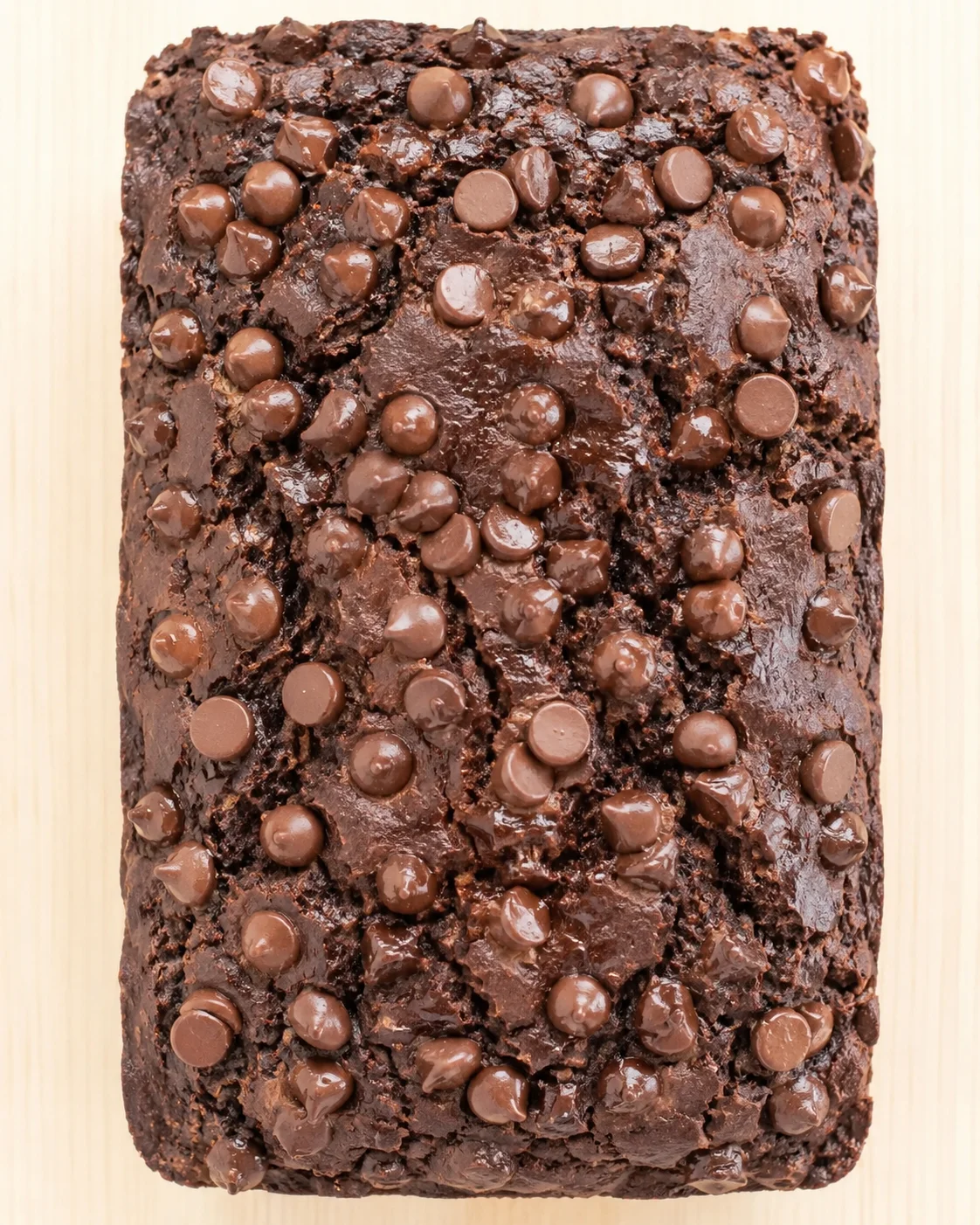 dense fudgy chocolate brownie studded with milk chocolate chips on a light wood surface