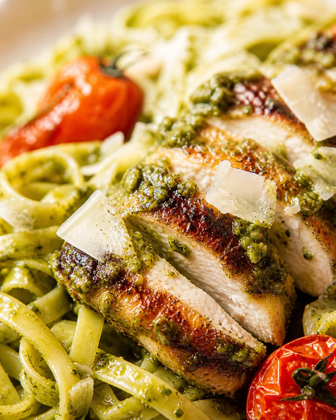 pesto-crusted-chicken-pasta Sliced pesto-coated chicken with green pasta and shaved parmesan on a sunlit plate