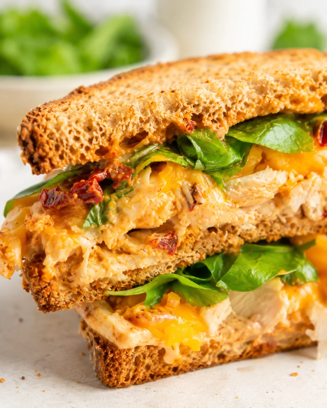 close-up of a toasted sourdough chicken melt with melted cheese and greens