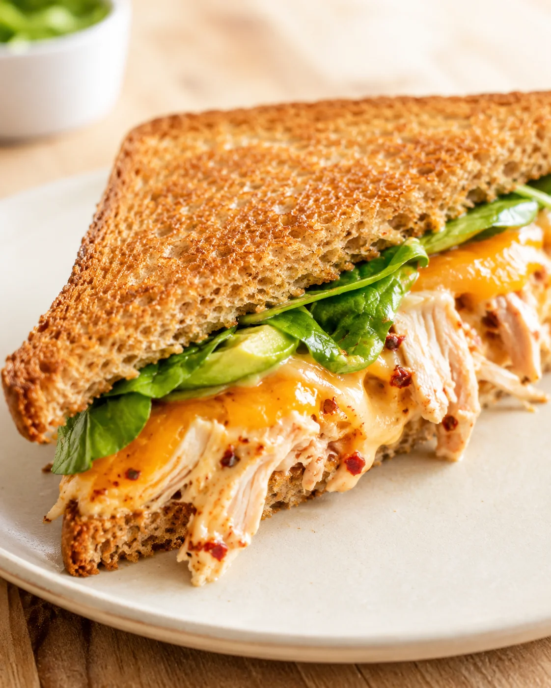 Crusty whole-grain chicken melt sandwich with melted cheese and greens on a plate.