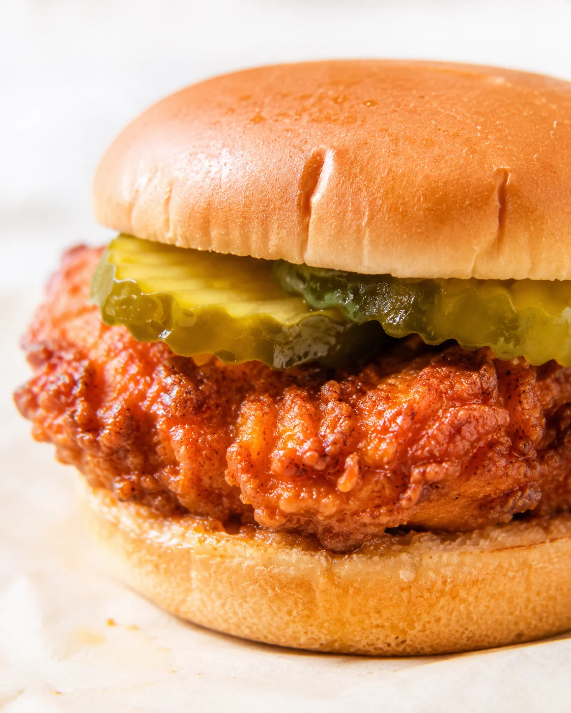 Close-up of a crispy fried chicken sandwich with pickles and melted cheese on a soft golden bun.