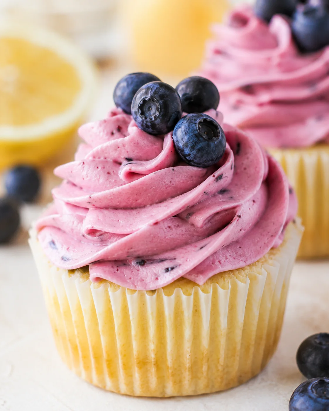 Close-up of a cupcake with pink blueberry-speckled frosting topped with blueberries.