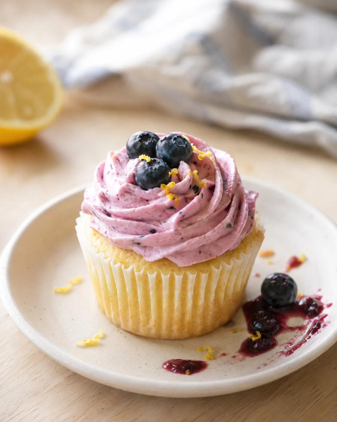 cupcake with pink blueberry frosting topped with blueberries on a light plate