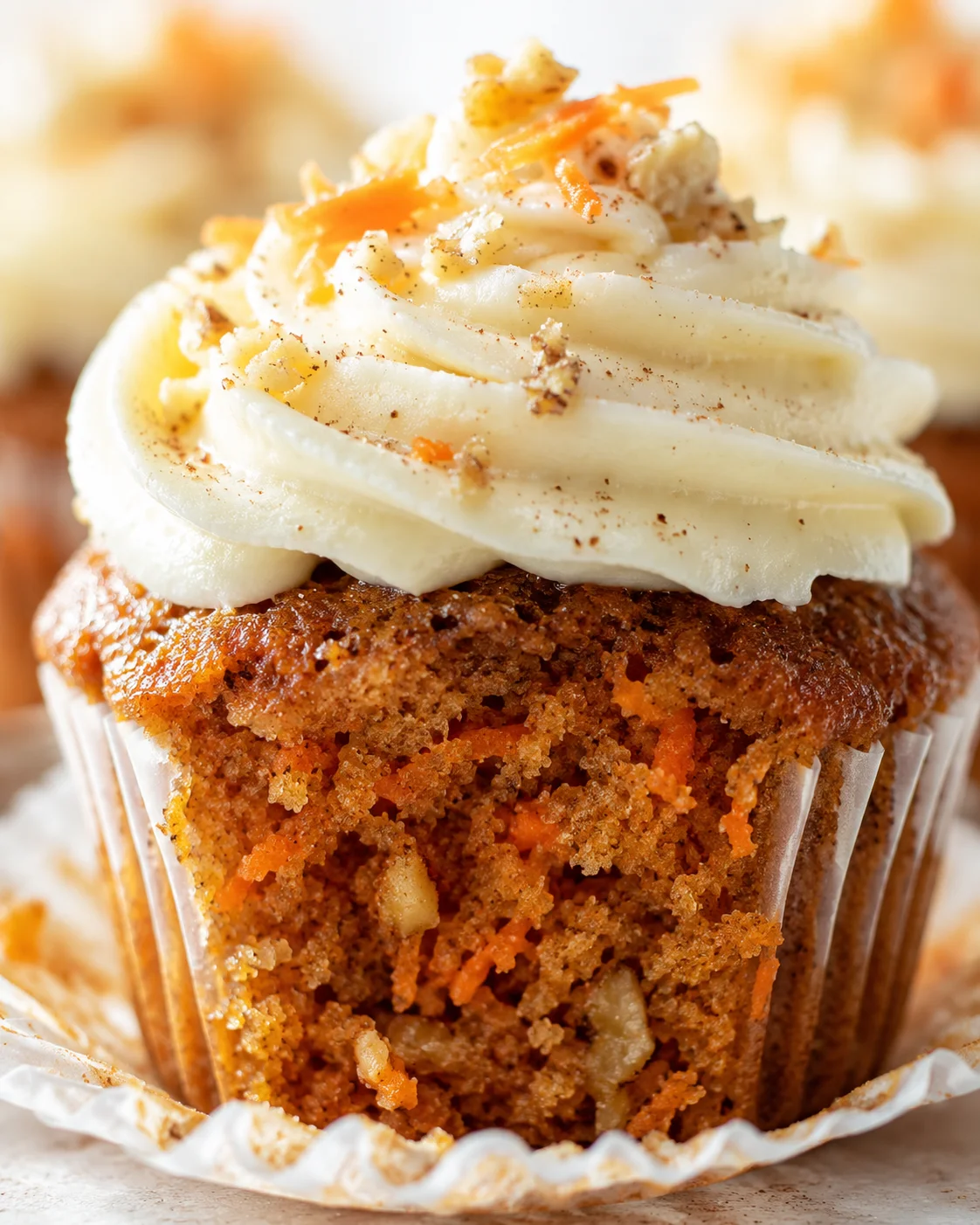 Close-up of a carrot cake cupcake with swirled cream cheese frosting and orange zest.