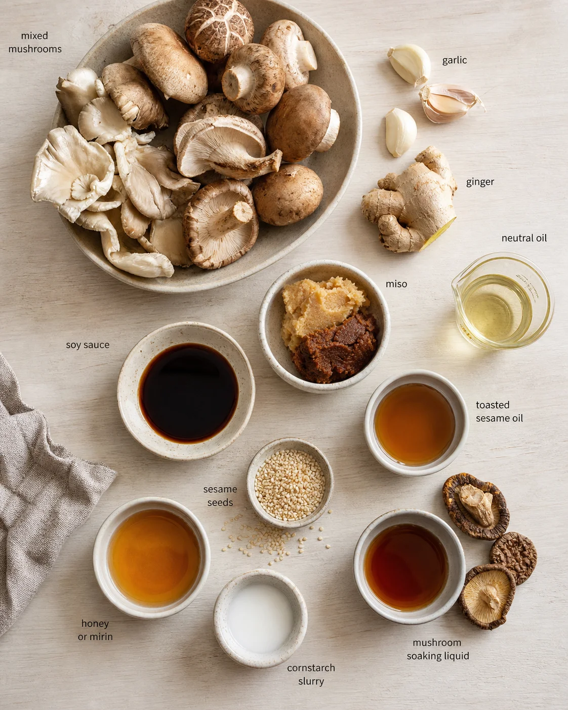 Flat lay of labeled miso soup ingredients including mushrooms, ginger, garlic, oils, and miso on a light wooden surface.