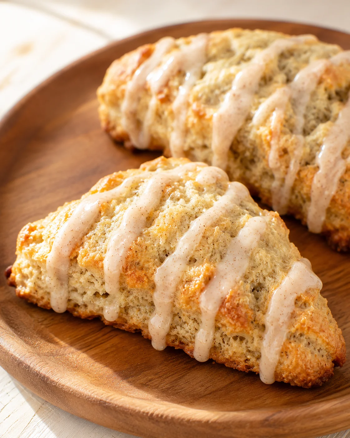 Two slices of banana bread on a wooden plate, drizzled with a creamy glaze.