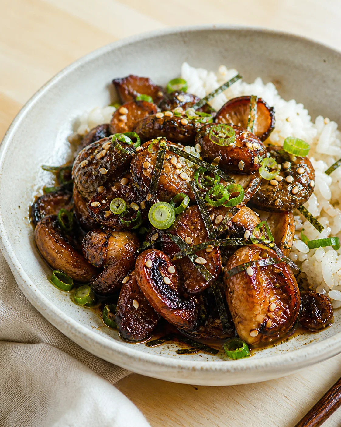 A bowl of glazed mushrooms atop white rice, garnished with sesame seeds, scallions, and nori.