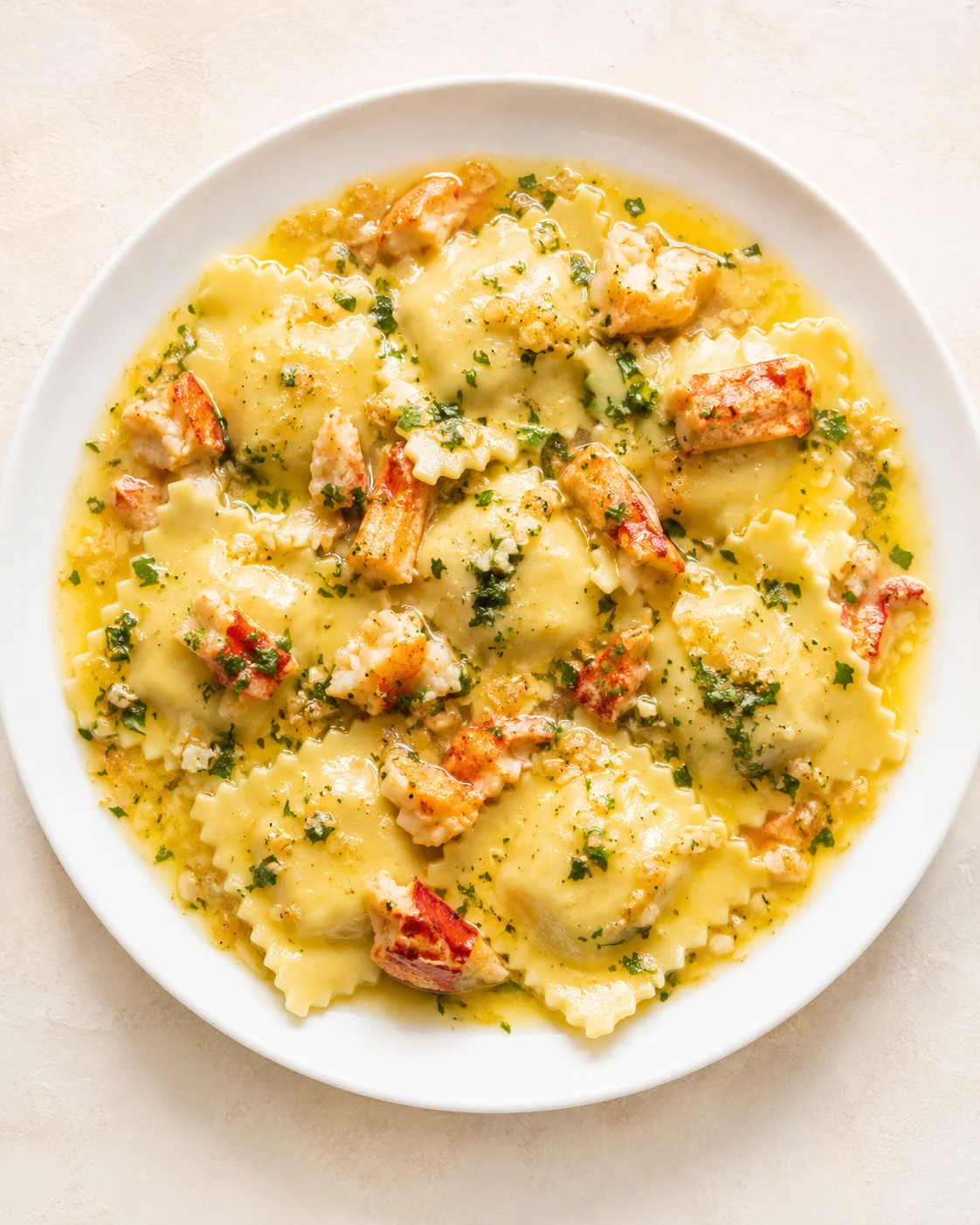 white plate of lobster ravioli in butter sauce with parsley garnish